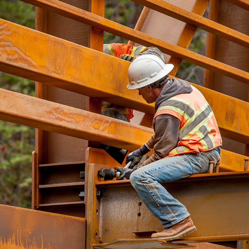 Steel workers puts the finishing fasteners on a bridge