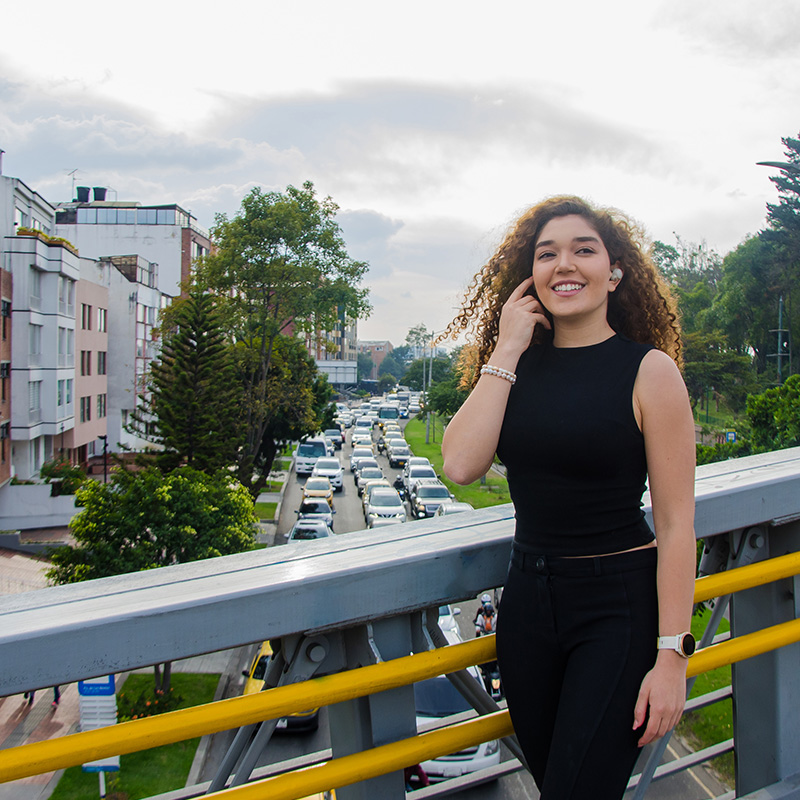 Portrait of woman with curly hair listening to music with wireless headphones in the street over a pedestrian bridge