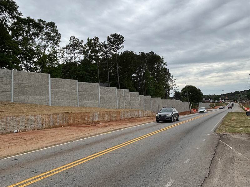 Roadway with concrete noise barrier and passing car.
